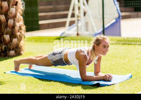 Perfect plank. Long side view of young Beautiful woman in sportswear faisant plank en étant debout sur la pelouse de l'avidité Banque D'Images