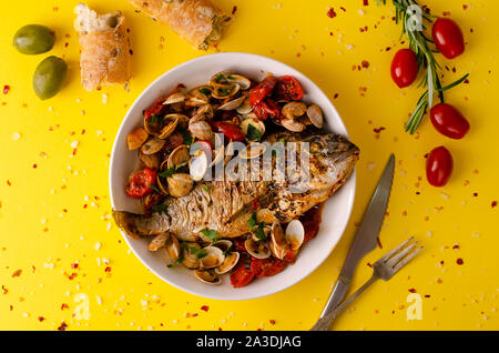 Concept cuisine méditerranéenne. La brème et les palourdes avec des tomates cherry,Pain aux olives et au romarin sur baclground jaune.Télévision lay, copy space Banque D'Images