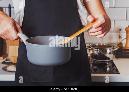 Man's hands close-up holding une casserole et remuer avec une cuillère de bois. Banque D'Images