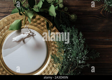 Lieu de Noël élégant avec des paramètres de branches naturelles de la décoration et de la plaque d'or. Figurine du renne sur le plat sur l'arrière-plan de tables en bois Banque D'Images