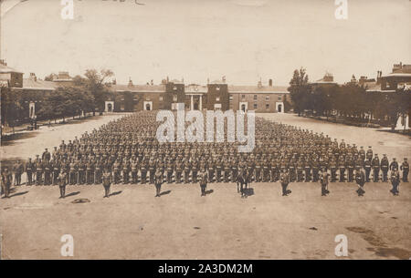 Vintage Début xxe siècle Carte postale photographique montrant un groupe de soldats de l'Armée britannique en Formation permanente sur un terrain de rassemblement au sein d'une grande caserne militaire.