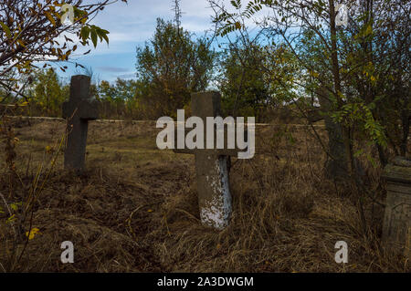 Vieille croix de pierre sur les pierres tombales du cimetière abandonné Banque D'Images