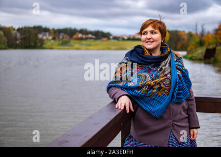 Grosse fille pensée sur le lac, temps nuageux, dans un beau rouge foulard Banque D'Images