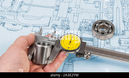 La mesure de la pièce d'acier par étrier dans la main de l'homme. Roulement à billes sur le dessin technique du moteur à combustion. Le contrôle de la qualité. Ingénieur avec outil de précision. Banque D'Images