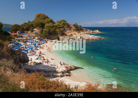 Les vacanciers à prendre le soleil sur des transats et chaises longues sous les parasols sur la plage de la station de vacances Kassiopi grec sur l'île de Corfou en Grèce Banque D'Images