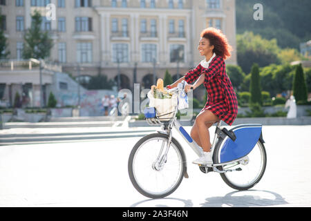 Curly red-haired woman riding bike après être allé au supermarché Banque D'Images