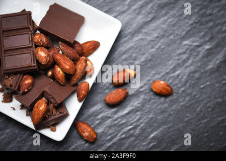 Amandes au chocolat noir de l'écrou sur plaque blanche sur le fond sombre / morceaux dessert sucré Bonbons et collations Banque D'Images