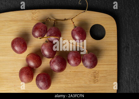 Groupe de onze entiers et frais de raisin pourpre rose sur une planche à découper en bambou sur flatlay pierre gris Banque D'Images