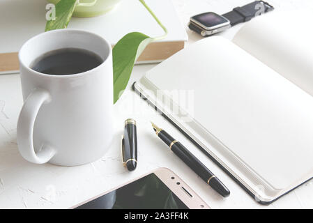 La main avec un stylo sur un bloc-notes papier à côté d'un livre et une tasse avec du café. Inspiration sur le lieu de travail avec copie vide de l'espace pour l'éditeur de texte. Banque D'Images