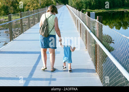 Enfant tenant la main et marcher avec grand-mère sur un pont sur une rivière Banque D'Images