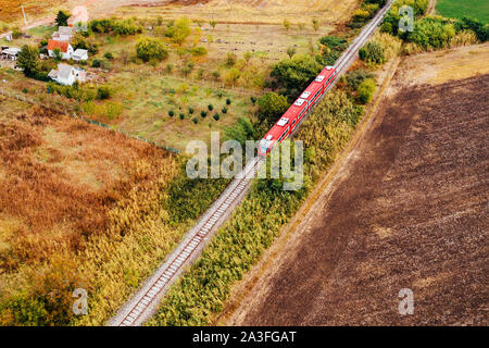 Le train de voyageurs rouge voyageant à travers campagne, vue aérienne du pov de drones à l'automne après-midi Banque D'Images