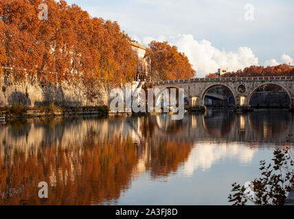 La rivière Tiber à Rome le jour ensoleillé de l'automne. Les arbres le long du bord de la rivière sont de belles couleurs d'automne, parfaitement reflétées dans l'eau encore. Banque D'Images