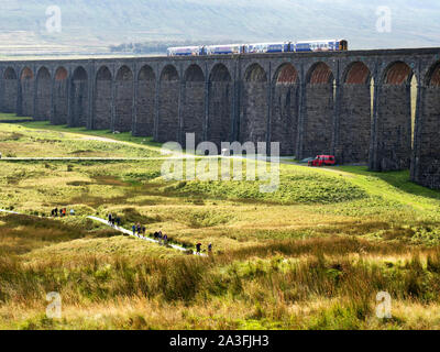 Les randonneurs sur un sentier au-dessous d'un train traversant le viaduc de Ribblehead Yorkshire Dales National Park en Angleterre Banque D'Images