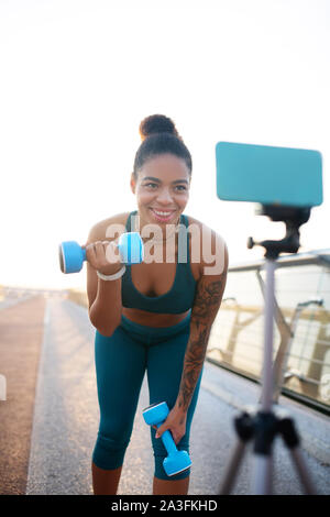 Femme faisant des exercices avec haltères longues lors du tournage d'blog Banque D'Images