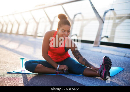 Femme avec cheveux bun étend les jambes tout en faisant du yoga Banque D'Images