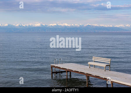 Pier avec bancs sur le lac Issyk-Koul avec une chaîne de montagnes avec des sommets enneigés à l'horizon contre un ciel nuageux Banque D'Images