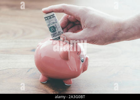 Close-up of male hand putting folded dollar bill in pink piggy bank on table en bois, et d'économiser de l'argent finances accueil concept Banque D'Images