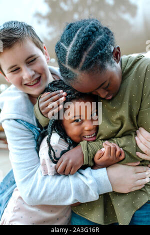 Frères et sœurs hugging multiraciale souriante jeune fille aux longues tresses Banque D'Images