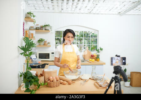 Jolie jeune femme d'origine asiatique food blogger travaille sur une nouvelle vidéo et d'expliquer comment cuisiner un plat Banque D'Images