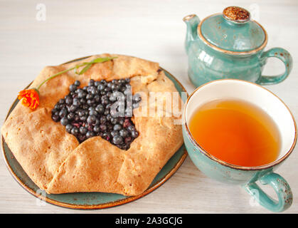 Tarte gâteau tarte Galeta galette de farine de grains entiers avec des bleuets sur un pays blanc table avec couleur turquoise tasse avec des fleurs. Vue de côté. Natural Banque D'Images