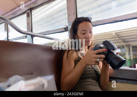 Young woman sitting at bus touristiques tout en utilisant votre appareil photo reflex numérique Banque D'Images