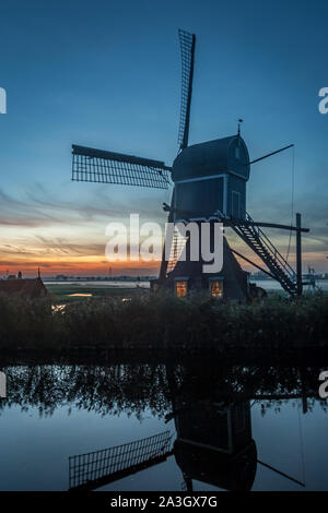 Moulin à vent près du village de Hazerswoude-Dorp, aux pays-Bas, recouvert d'un canal de polder. Couleurs crépusculaires au-dessus des berges de brouillard dans la campagne néerlandaise. Banque D'Images