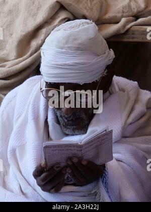 L'Éthiopie, région d'Amhara, un vieil homme vêtu de blanc se lit des prières en face d'une église de Lalibela Banque D'Images