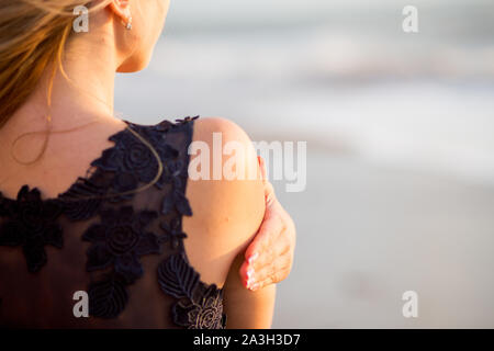 Belle jeune femme avec des cheveux bouclés blond doré en plein air au coucher du soleil avec son dos à nous. Banque D'Images