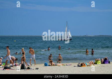 La France, l'Hérault, Meze, vacanciers sur une plage de la lagune de Thau avec un voilier dans l'arrière-plan Banque D'Images