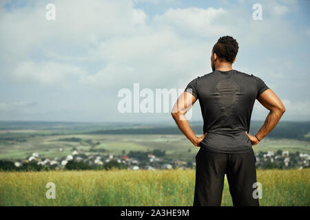 Vue arrière de l'Afrique de l'musculaire sportsman portant en noir T-shirt et short noir. Beau, fort, athletic homme debout et posant à l'extérieur. La tenue de l'athlète les mains sur les hanches. Banque D'Images