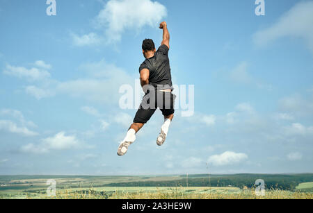 Vue arrière de l'unité africaine, musculaire élevé. saut sportif Le port sportif en noir T-shirt et un short, chaussettes blanches et chaussures de posant sur fond de ciel bleu. Banque D'Images