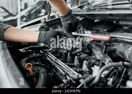 L'homme qualifié en noir des gants sales se dévisse ancien bougies de moteur de voiture par clé pour les transformer en nouveaux.Auto mechanic proficiently exerce ses fonctions de base en service centre Banque D'Images