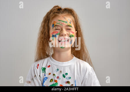 Petite fille en t-shirt blanc, avec visage peint fait des grimaces tout en se posant isolé sur blanc. Art Studio. Close-up. Banque D'Images