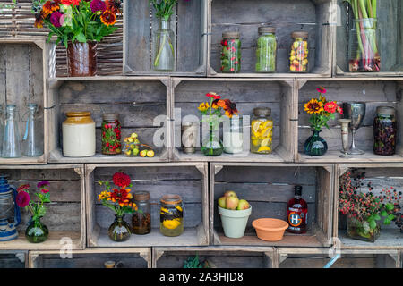 Pots de gin au four à l'ancienne infusés de fruits et de noix avec vases de fleurs coupées dans une caisse en bois exposée à un salon de l'automne, Royaume-Uni Banque D'Images