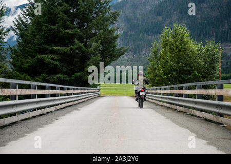 Une femme rides sa motocyclette sur un pont, sur une journée d'été.