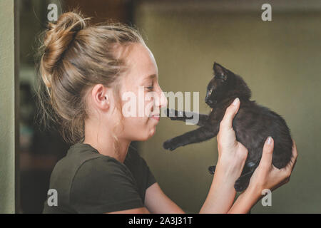 Petit chaton noir à pattes teen girl's nez comme elle le tient et sourires Banque D'Images