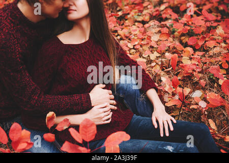 Couple portée dans les vêtements de style automne pulls famille regarder assis sur le paysage d'automne. Feuillage jaune couverte de forêt. Automne marcher à l'extérieur. Banque D'Images