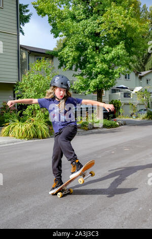 Jeune garçon aux cheveux long sur la planche à roulettes rue résidentielle. Banque D'Images