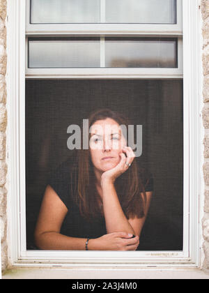 Femme regardant par la fenêtre ouverte avec menton reposant sur la main. Banque D'Images