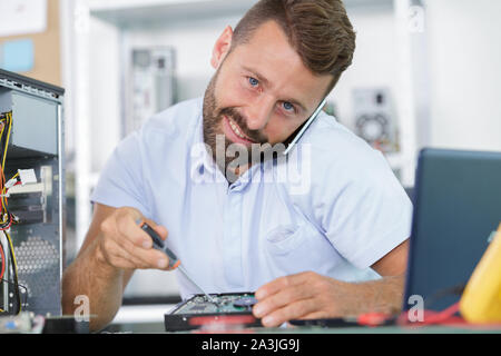 Smiling man sur le téléphone à l'aide de tournevis en pc fixation Banque D'Images
