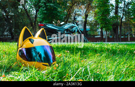 Le casque jaune d'un biker girl d'une moto avec miroir et les oreilles se trouve sur l'herbe verte dans le contexte d'une moto gris Banque D'Images