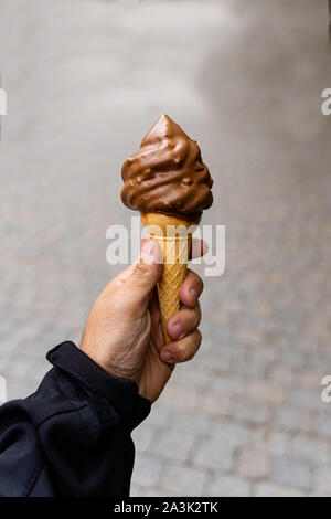 Man holding feux de glace au chocolat crème glacée à la main, très arrière-plan flou, faible profondeur de champ. Fond sombre. Banque D'Images