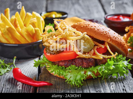 Cheeseburger avec fromage cheddar, oignons frits croustillants, laitue, tomates, cornichons, sur une table en bois rustique, close-up Banque D'Images