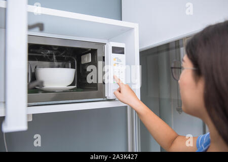 Les femmes réchauffer des aliments par l'utilisation de four à micro-ondes avec bol en céramique en verre. Banque D'Images