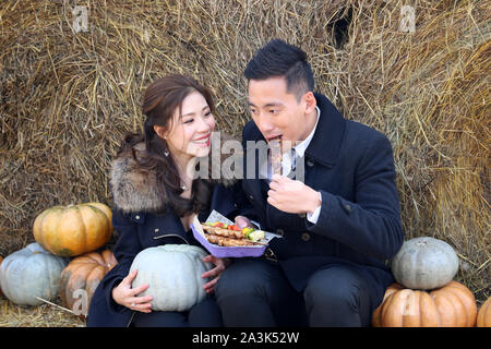 Happy asian couple manger un kebab assis sur une pile de citrouilles décorées avec du foin. Les touristes sur la Place Rouge au cours de l'automne d'or du festival Banque D'Images