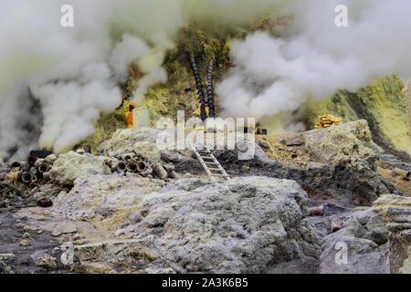 Exploitation minière de soufre dans le cratère du Mont Ijen, Java Est, Indonésie. Gaz volcanique blanche passant de fissures dans le sol. Pipes dans l'arrière-plan. Banque D'Images