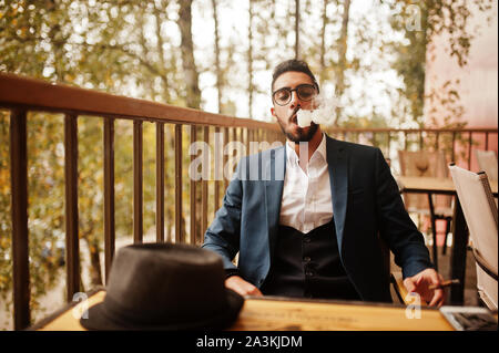 Bien habillé beau homme arabe à cigares fumée balcon de pub. Banque D'Images