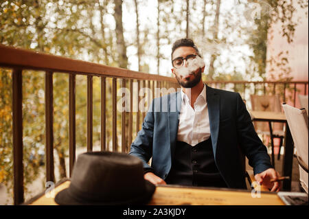 Bien habillé beau homme arabe à cigares fumée balcon de pub. Banque D'Images