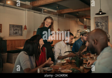 Bistro sympathique serveuse parlant avec une table de clients souriants Banque D'Images