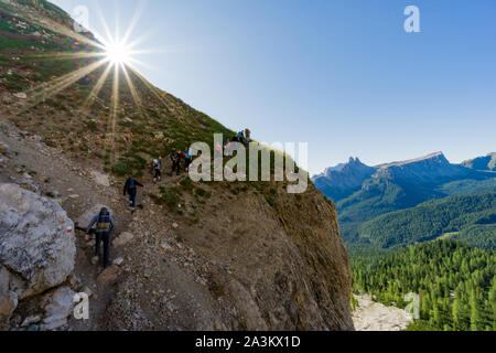 Grand groupe de jeunes randonneurs qui monte un sentier de randonnée escarpé avec le soleil qui brille au-dessus d'eux et vue fantastique sur le paysage de montagne derrière Banque D'Images